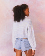 Back view of blue and cream cropped pullover sweater with textured knit and crew neckline. Long cuffed sleeves and ribbed hem above waistline.