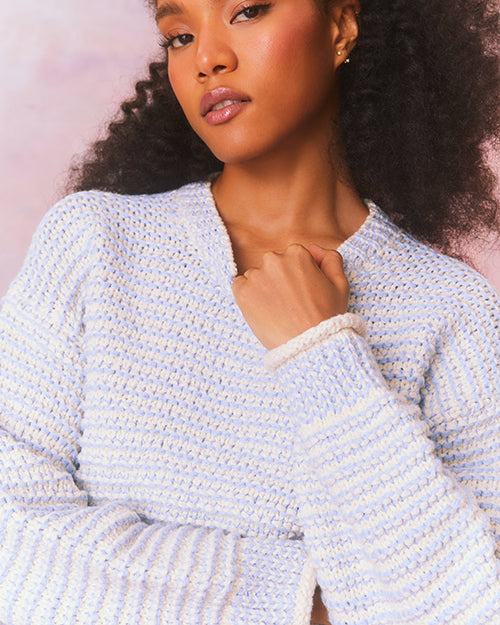 Close-up of blue and cream cropped pullover sweater with textured knit and crew neckline. Long cuffed sleeves and ribbed hem above waistline.