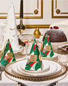 A festive holiday table setting featuring a white tablecloth with a gold-rimmed plate at the center, flanked by silverware. On the plate rests a  packaging is designed to resemble a Christmas tree, with a geometric pattern in shades of green, red, and white. The scene conveys an opulent holiday feast ambiance.