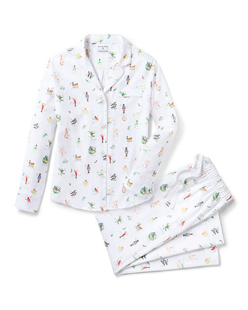 White pajama set featuring a button-up top with a collar, long sleeves, and a left chest pocket, paired with matching pants with an elastic waistband. The fabric is adorned with colorful, whimsical illustrations of animals and people engaged in various activities.