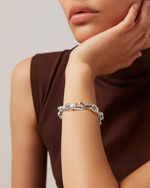 The  woman has her left hand under her chin with a silver chain bracelet on her wrist.