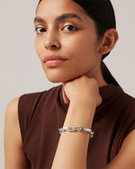 An up close image of a woman with her left hand under her chin, wearing silver chain bracelet