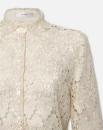 Close-up of a beige short-sleeved, lace blouse with a floral pattern. The blouse features a collar and a front button closure, and scalloped edges on the sleeve and hem. 