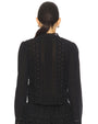 Back view of a black long-sleeve blouse featuring intricate eyelet embroidery with small stud embellishments, vertical lace-like panels, and a scalloped neckline detail.