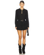 Front view of a black long-sleeve mini dress featuring a scalloped neckline, button-down front, intricate eyelet embroidery with small stud embellishments, a tiered skirt with scalloped hem, and a black belt with a gold buckle at the waist. Styled with black mid-calf boots and a small black handbag.