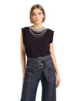 Woman wearing a black top with embellishments and blue jeans on a light background