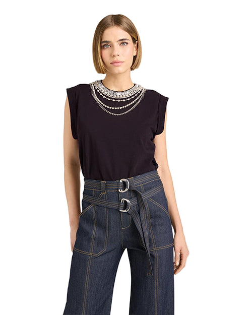 Woman wearing a black top with embellishments and blue jeans on a light background