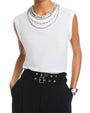 Model wearing a white sleeveless top with layered silver chain neckline, paired with black high-waisted pants featuring double belts and silver eyelets, accessorized with a silver bracelet.