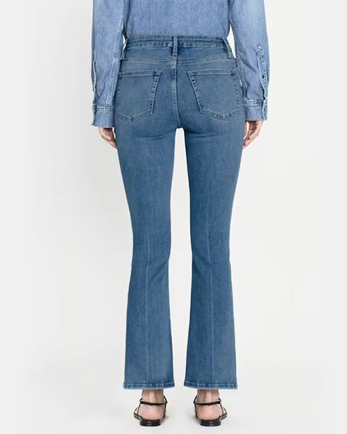 Back view of person wearing slim fit jeans with a medium wash and are high-waisted with a slight flare at the ankles. Jeans are styled with black strappy sandals and a denim long-sleeve button-up shirt.