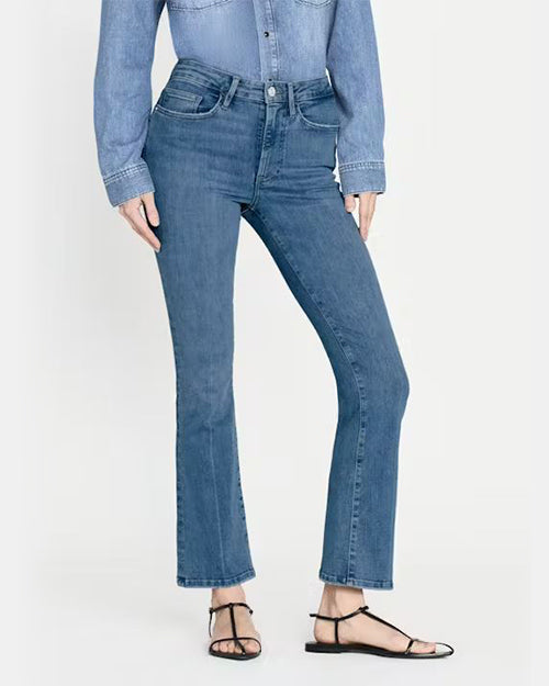 Slim fit jeans with a  medium wash and are high-waisted with a slight flare at the ankles. Jeans are styled with black strappy sandals and a denim long-sleeve button-up shirt. 