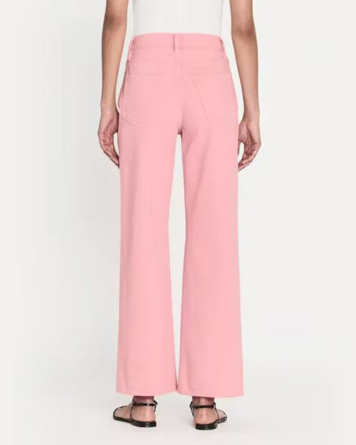 A back view of a model wearing high-waisted pink denim trousers with a straight cut fit and raw hem paired with a white top. The model styles the pants with black open-toe sandals.