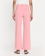A back view of a model wearing high-waisted pink denim trousers with a straight cut fit and raw hem paired with a white top. The model styles the pants with black open-toe sandals.