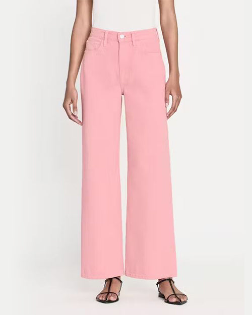 A pair of light pink, wide-leg trousers displayed on a model. The trousers have a ultra high rise with a silver button closure and are made of denim. Trousers are fitted through the hips and wide through the legs. The model styles the pants with black open-toe sandals.