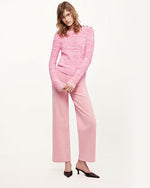 A model wearing high-waisted pink denim trousers with a straight cut fit and raw hem paired with a pink textured top, paired with black pointed-toe heels. 
