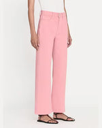 A side view of a model wearing high-waisted pink denim trousers with a straight cut fit and raw hem paired with a white top. The model styles the pants with black open-toe sandals.