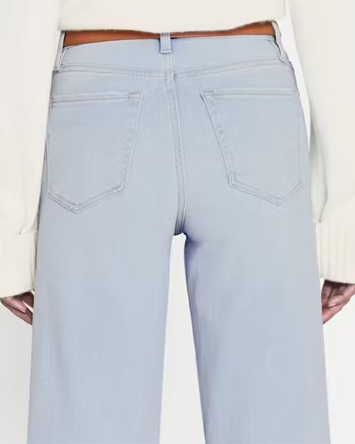 A close-up image of the back of high-waisted  light blue denim jeans. Jeans are paired with brown belt and white top.