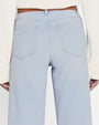 A close-up image of the back of high-waisted  light blue denim jeans. Jeans are paired with brown belt and white top.