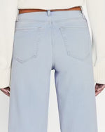 A close-up image of the back of high-waisted  light blue denim jeans. Jeans are paired with brown belt and white top.