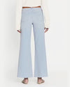 Back view of model wearing high waisted light blue flared jeans. The jeans are frayed at the hem and paired with white top and brown belt.