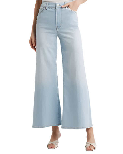 A person is wearing light blue high-waisted wide-leg jeans and white open-toe sandals. The jeans have a button and zipper closure, front pockets, and a slightly faded wash. The person's upper body is not visible in the image.