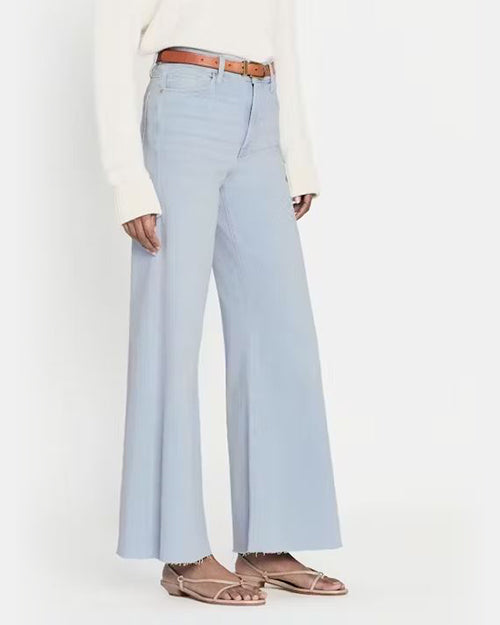 Side view of model wearing high waisted light blue flared jeans. The jeans are frayed at the hem and paired with white top and brown belt.