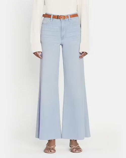 A person wearing high waisted light blue flared jeans styled with a white top and a brown belt. The person is also wearing open-toed brown sandals. The jeans feature a frayed, swingy hem that showcases both heels and flats. The background is plain and white, emphasizing the outfit.