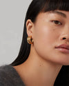 Close-up of a person with long, straight black hair wearing a grey fuzzy sweater and a gold hoop earring. 