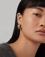Close-up of a person with long, straight black hair wearing a grey fuzzy sweater and a gold hoop earring. 
