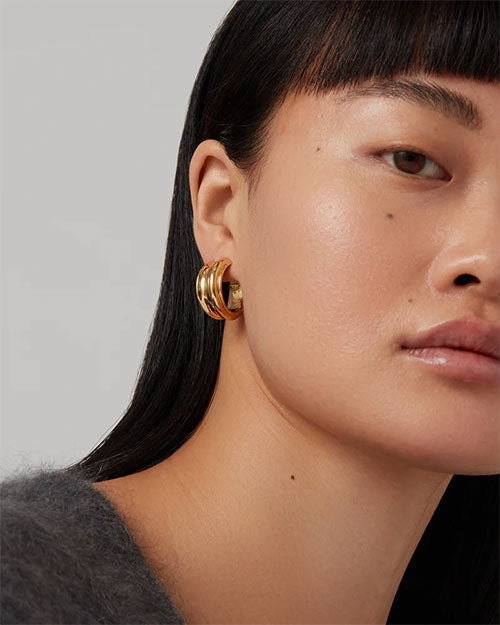 Close-up of a person with long, straight black hair wearing a grey fuzzy sweater and a gold hoop earring. 