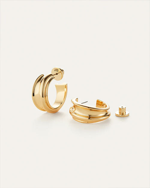 Pair of gold hoop earrings with a smooth, shiny finish; one earring stands upright showing 'JB' engraved on the back, while the other lies down with its back detached beside it.