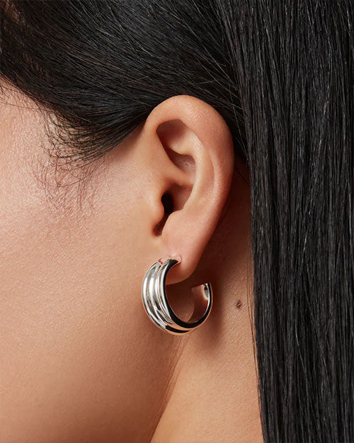 Close-up of an ear wearing a smooth, shiny silver hoop earring; straight dark hair partially visible.