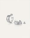 Pair of silver hoop earrings with a modern, chunky design; one earring stands upright showing the post and 'JB' engraved on the back, while the other lies down with its back detached beside it.