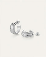 Pair of silver hoop earrings with a modern, chunky design; one earring stands upright showing the post and 'JB' engraved on the back, while the other lies down with its back detached beside it.