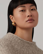 Person with black hair wearing a beige knitted sweater and gold hoop earrings.