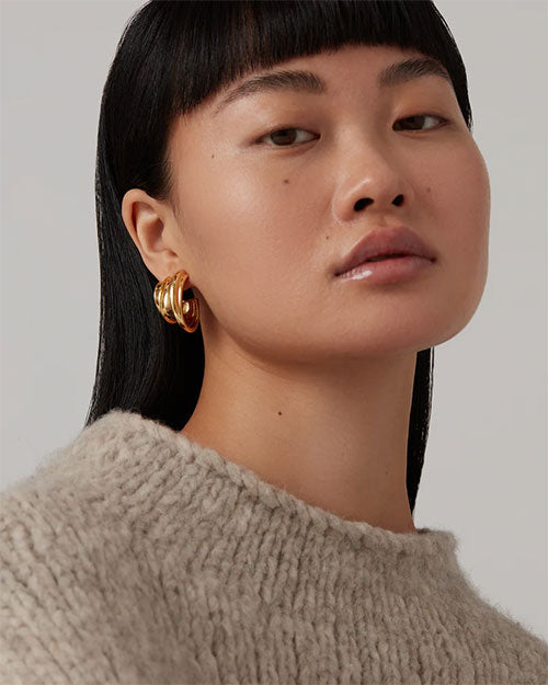 Person with black hair wearing a beige knitted sweater and gold hoop earrings.