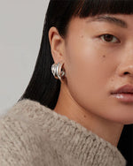 Close-up of a person's face, focusing on the left side of the head; the person has straight, dark hair and is wearing a textured, light-colored garment.