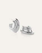 Pair of silver hoop earrings with a modern, layered, and curved design; smooth reflective surface, one earring upright and the other lying on its side.