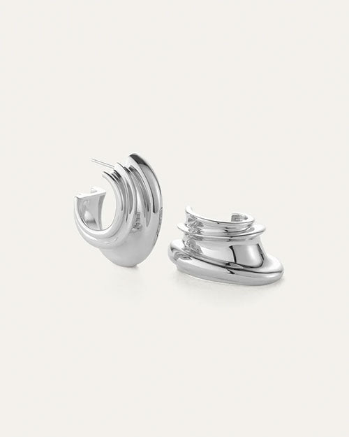 Pair of silver hoop earrings with a modern, layered, and curved design; smooth reflective surface, one earring upright and the other lying on its side.