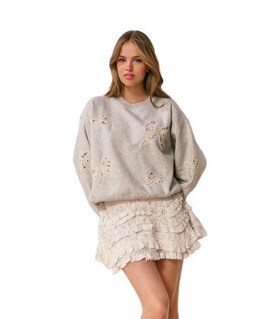 Woman wearing a gray sweatshirt with bow designs and a lace skirt on a plain background