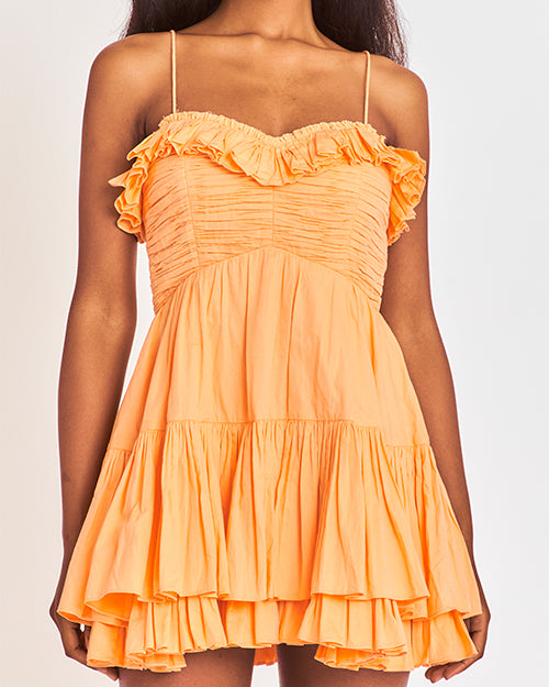 Model wearing a bright orange dress with ruffled details on the top and bottom, standing against a plain background.