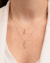 Close-up of a person’s neck wearing a white collared shirt and two layered gold necklaces. The top necklace has a pink ribbon charm and bottom necklace is a 'love' script.