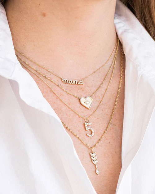 A close-up image of a person wearing a white collared shirt, wearing four layered necklaces.