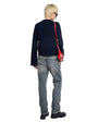Person standing with their back to the camera, wearing a black long-sleeve shirt, light blue jeans, and black shoes. They have blonde hair and are carrying a red shoulder bag on the left side.