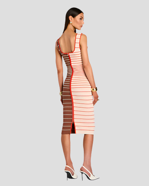 The backside view of a model wearing an over the shoulder strap, just below knee-length dress with a fitted silhouette. The dress is half white/cream and half brown and features horizontal stripes in varying shades of red and white, with a vertical red stripe running down the center front. The person is also wearing white high-heeled shoes and has gold bracelets on both wrists and gold hoop earrings. 