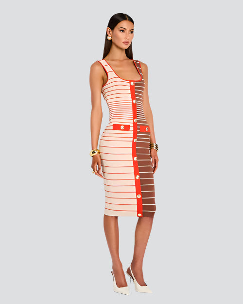 A model is seen wearing an over the shoulder strap, just below knee-length dress with a fitted silhouette. The dress is half white/cream and half brown and features horizontal stripes in varying shades of red and white, with a vertical red stripe running down the center front. The red stripe is adorned with medium sized buttons. The person is also wearing white high-heeled shoes. Additionally, the person has gold bracelets on both wrists and gold hoop earrings. 
