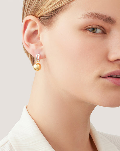 A close-up on a earring featuring a two-tone design. Earring consists of a small silver hoop connected to a larger, polished gold sphere. 
