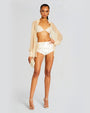 Model wearing a sheer nude button down long top, underneath, model wearing sequin ivory short shorts and bralette, and matching shoes and clutch.