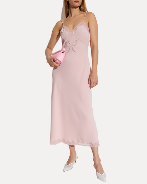 Woman wearing a pink slip dress holding a clutch on a white background