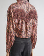 Back view of a person wearing a long-sleeved shirt with a colorful paisley pattern and fringe detailing across the upper back and shoulders, paired with dark-colored jeans.