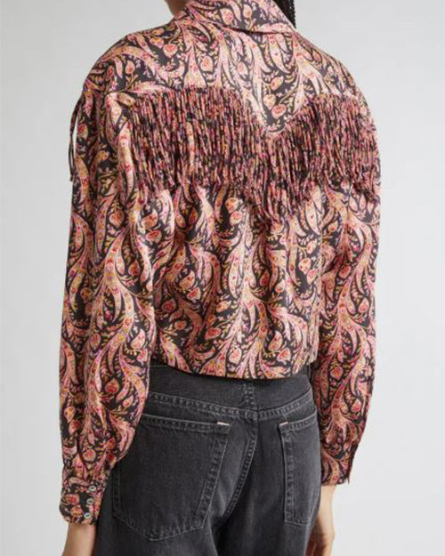 Back view of a person wearing a long-sleeved shirt with a colorful paisley pattern and fringe detailing across the upper back and shoulders, paired with dark-colored jeans.